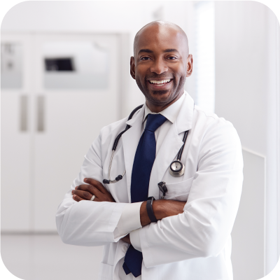 African American male doctor smiling with arms crossed in a hospital hallway.