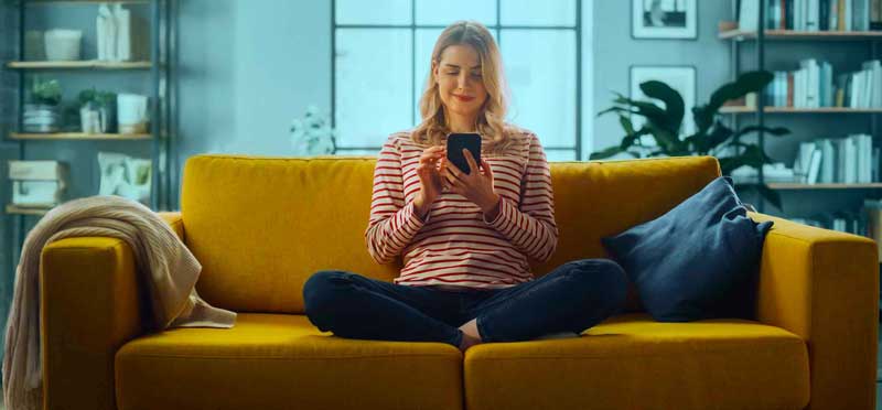 Female Using Smartphone in Stylish Living Room while Sitting on a
         Cozy Couch Sofa.