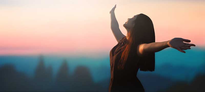 Happy woman raised hand on blurred mountain sunrise background.