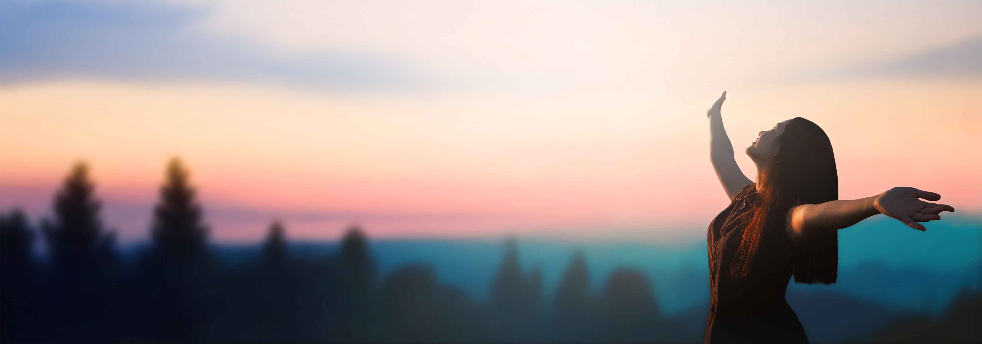 Happy woman raised hand on blurred mountain sunrise background.