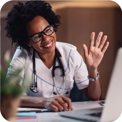 Happy African American doctor waving while making a video call over laptop.