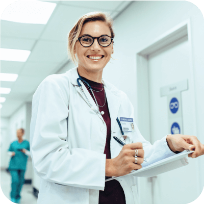 Female physician in hospital corridor writing on a clipboard.