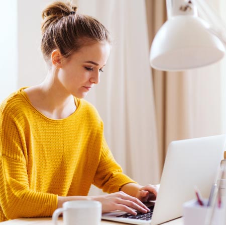 Woman in yellow sweater using a laptop.