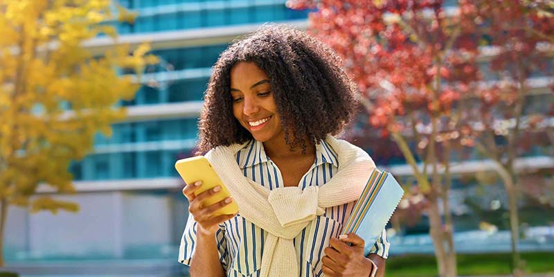 Woman holding a phone and a notebook while walking outside near an office building.