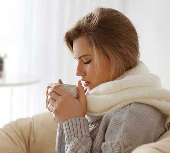 Woman wearing a scarf and wearing a sweater holding a cup with both hands.
